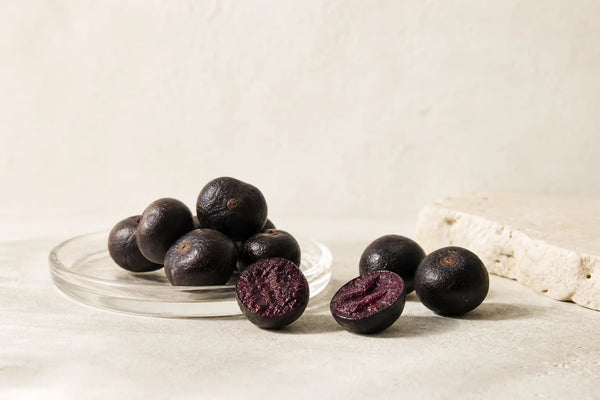 Whole and halved acai berries with visible dark purple pulp on a neutral background